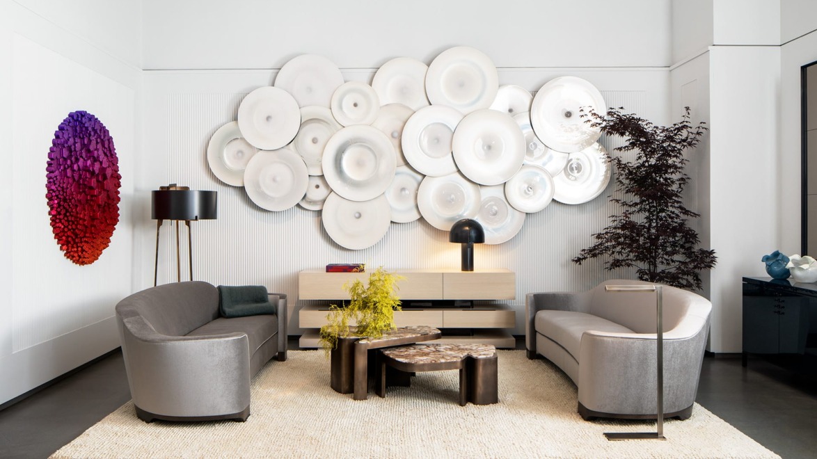 Modern living room with abstract wall art, gray sofas, circular coffee tables, black floor lamp, and decorative plants.