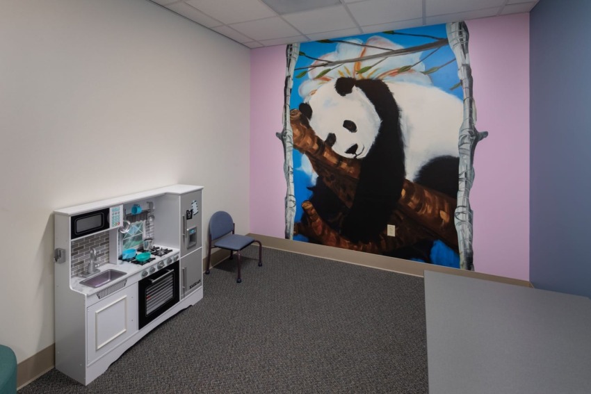 playroom corner with a toy kitchen and a large wall mural of a panda bear climbing a tree