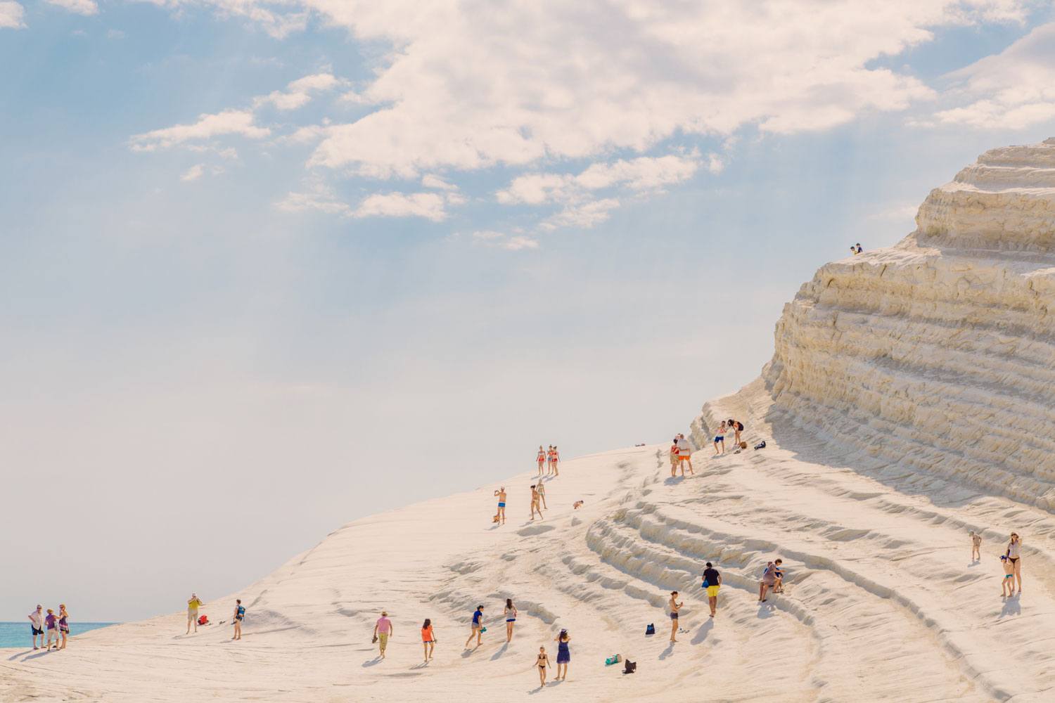 People walking on white, natural limestone terraces under a partly cloudy sky.