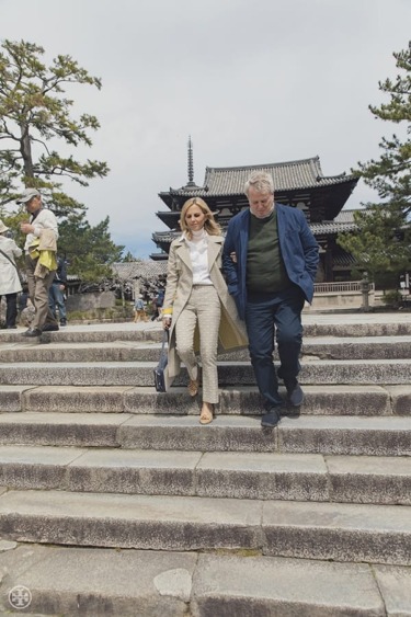 People walking down stone steps in front of a traditional Japanese building with trees in the background.
