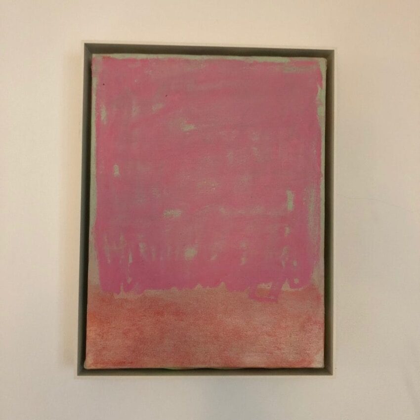 Abstract painting with shades of pink and red on a canvas, framed in a simple, thin border, against a neutral wall.