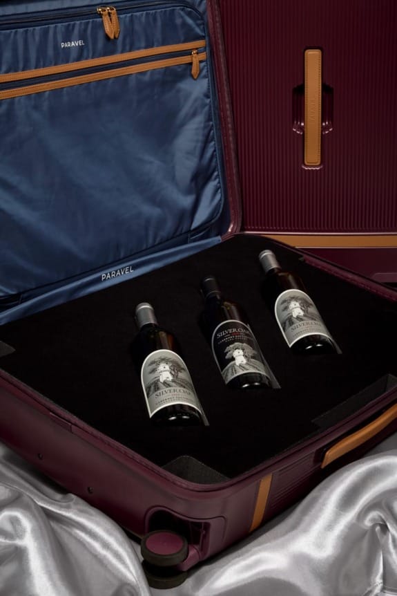 Open suitcase with three wine bottles in a cushioned compartment, featuring a navy interior and burgundy exterior.