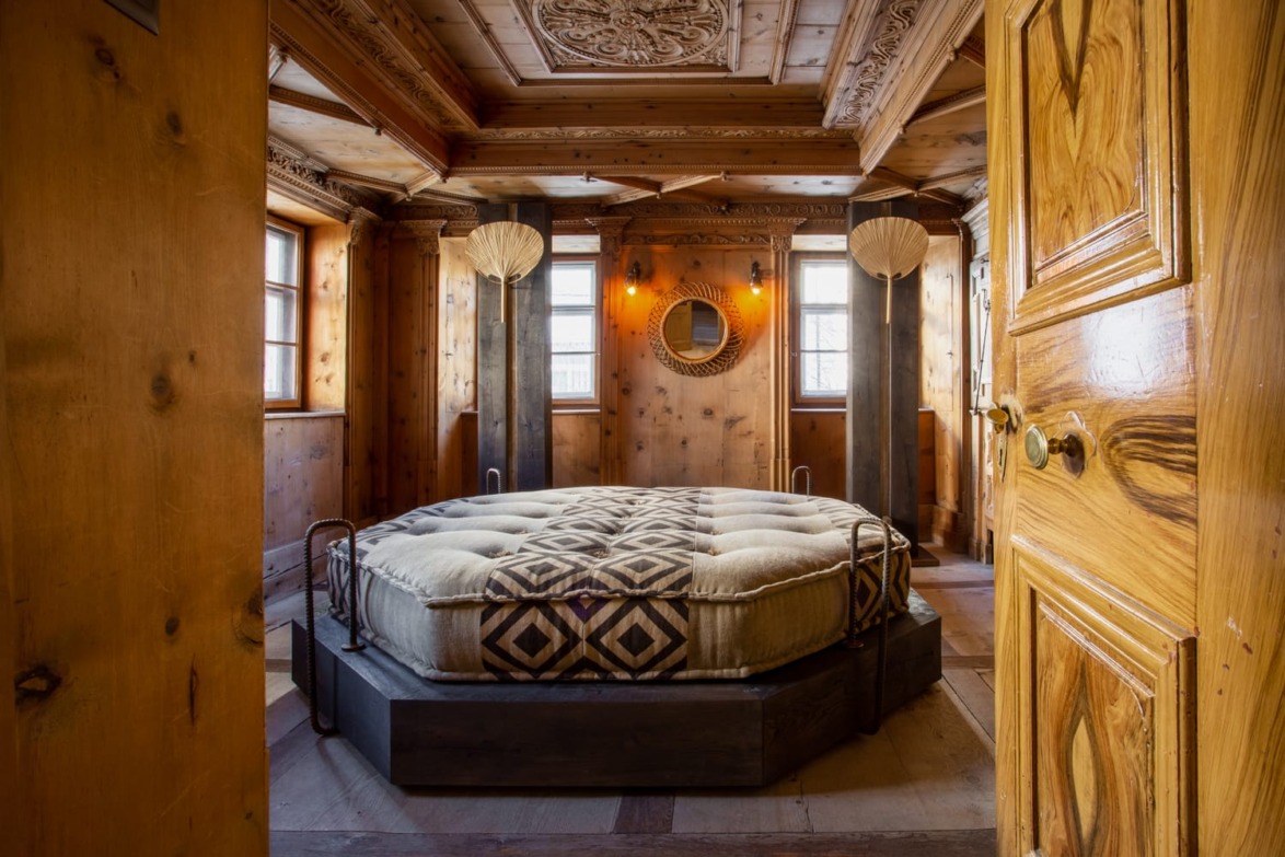 Rustic bedroom with round bed, wooden walls, carved ceiling, and decorative mirror, creating a cozy and inviting atmosphere.