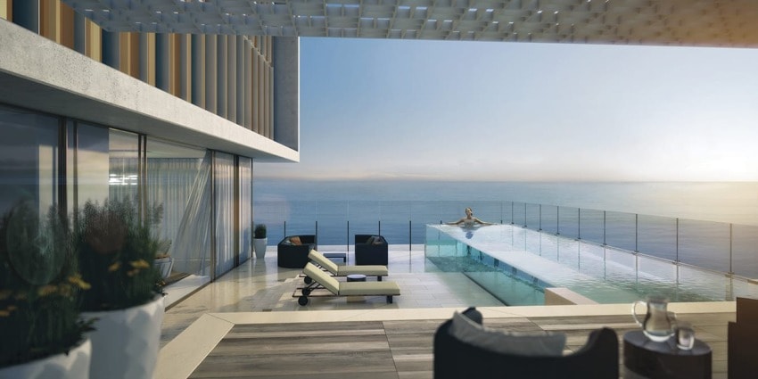 Modern beachfront terrace with infinity pool, lounge chairs, and ocean view at sunset.