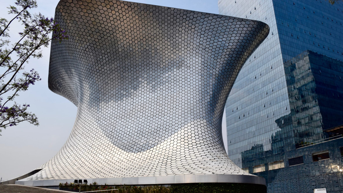 Modern, futuristic building with hexagonal pattern, curved structure, and reflective surfaces under a clear blue sky.
