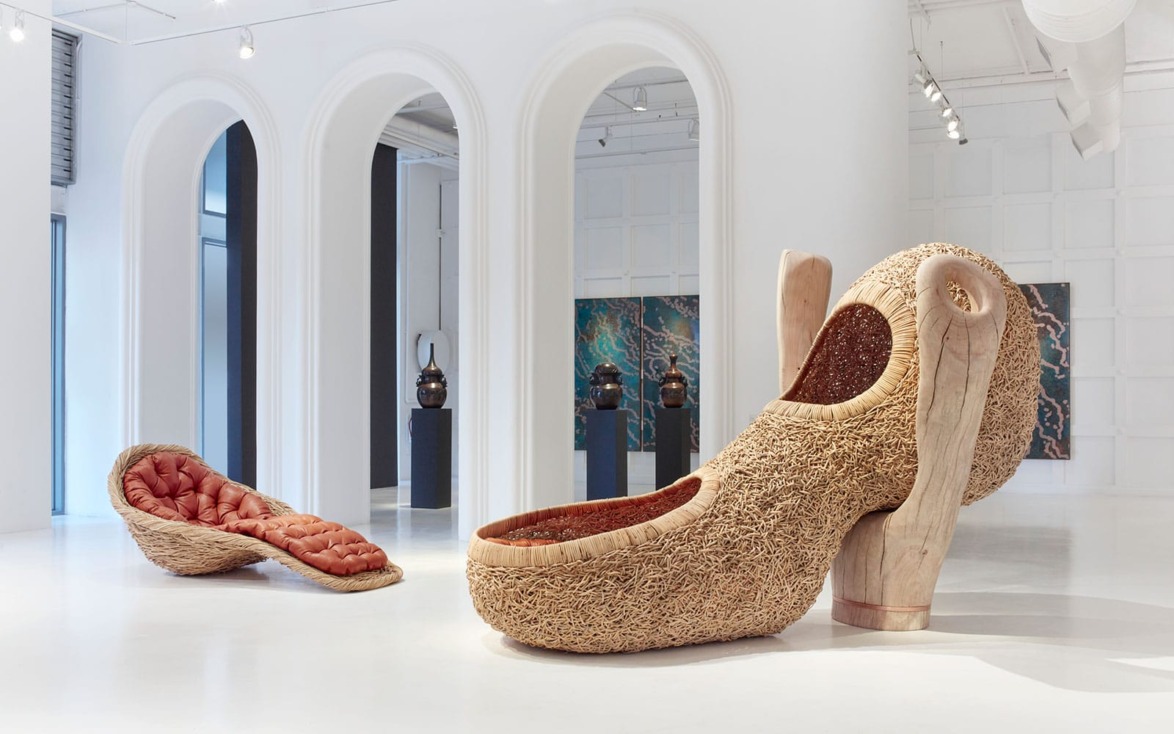 Modern art exhibit featuring two large, creatively designed chairs with organic shapes and textured surfaces in a bright gallery space.