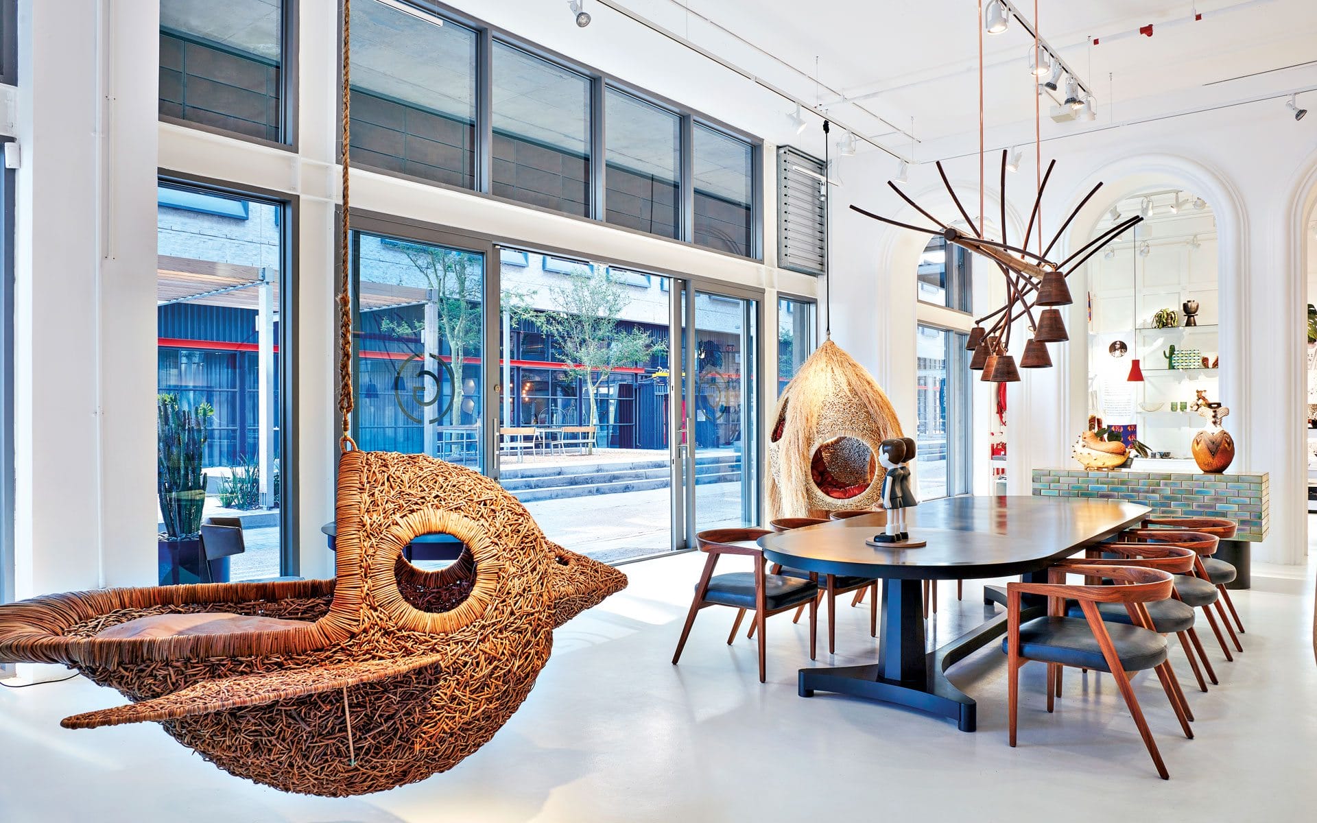 Modern showroom with unique wicker chairs, wooden dining table, and large windows giving view to the outside street scene.