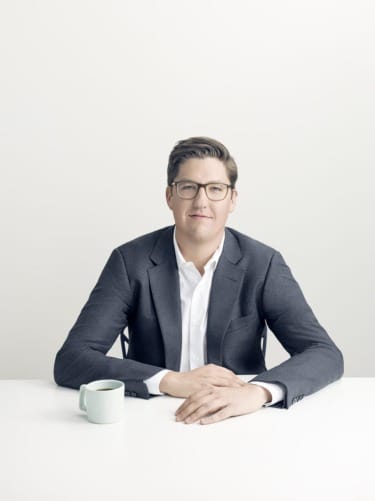 Person in glasses and suit sitting at a table with a green mug.