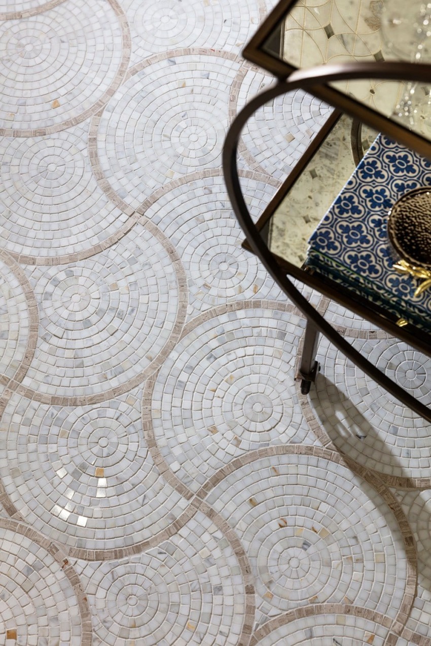 Intricate circular mosaic tile pattern on a floor next to a glass table with decorative items on top.