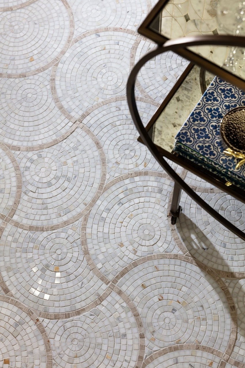 Intricate circular mosaic tile pattern on a floor next to a glass table with decorative items on top.