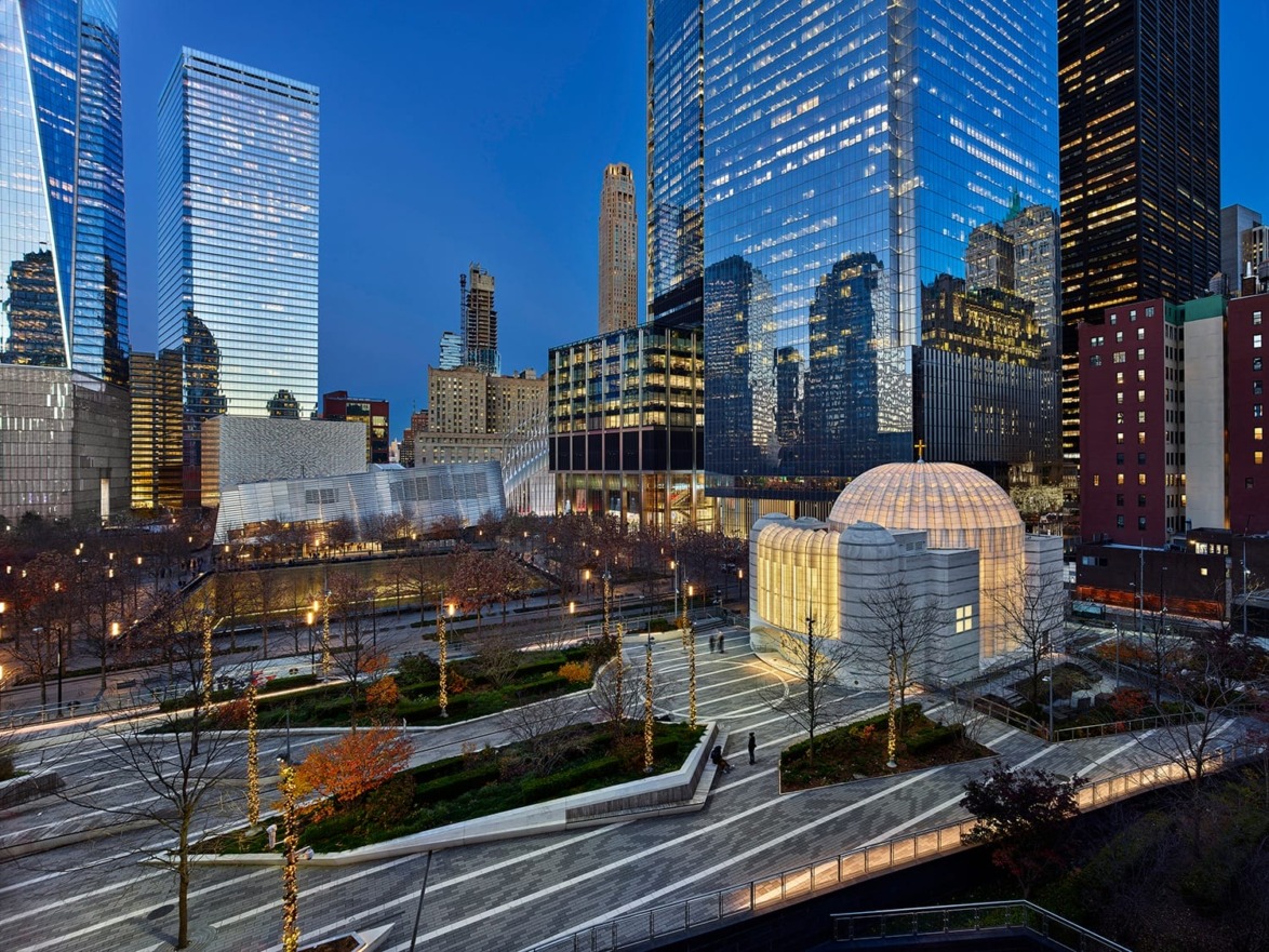 Evening view of modern cityscape with tall glass buildings and a lit dome structure, trees, and pathways in foreground.