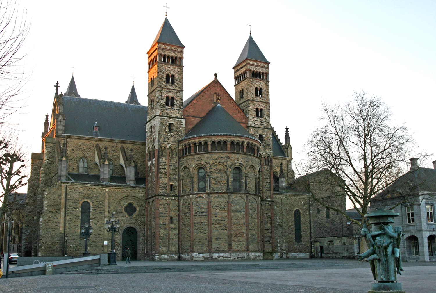 Historic stone church with two tall towers, featuring detailed architectural elements and a tree in a quiet plaza setting.