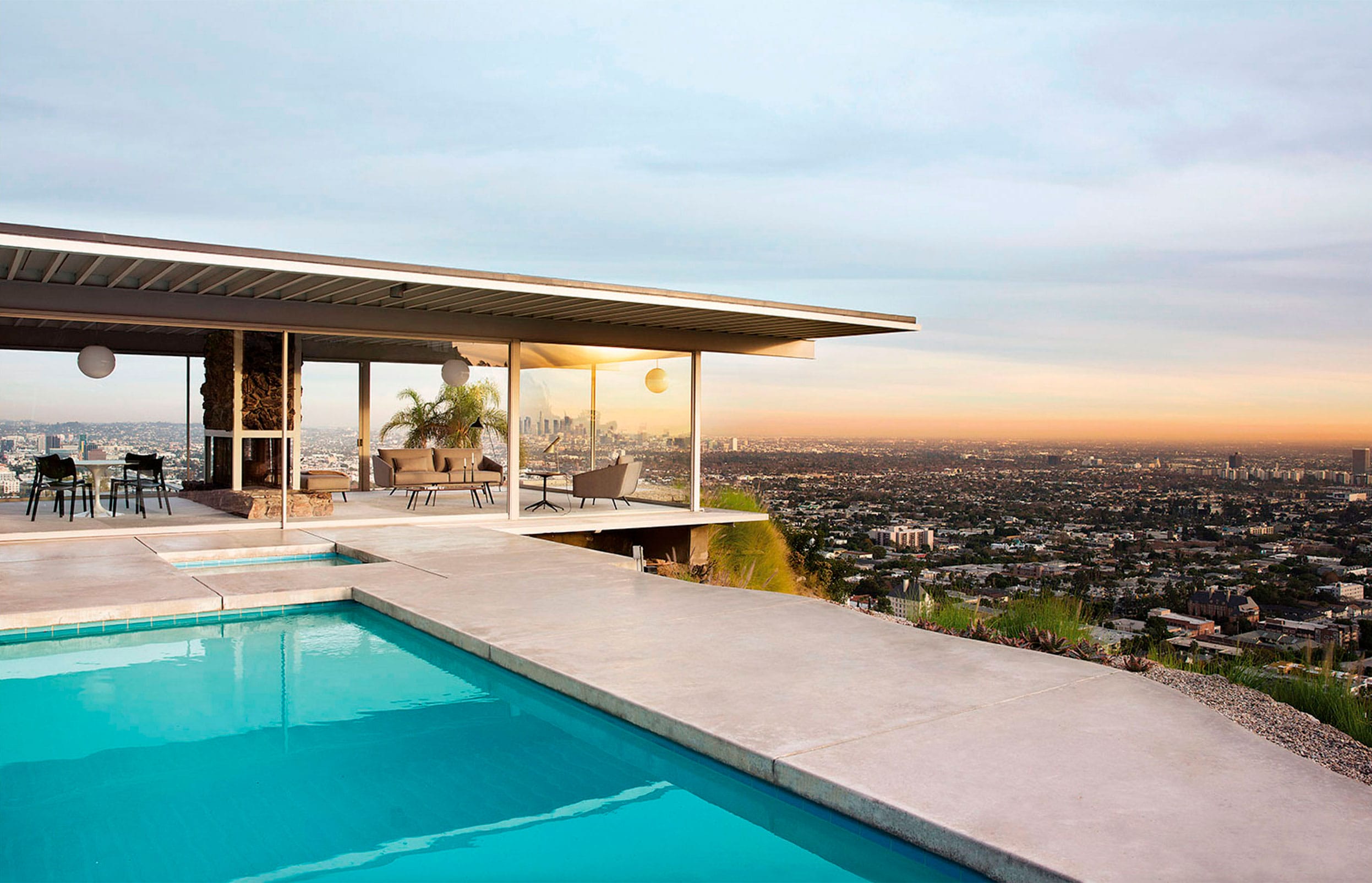 Modern house with pool overlooking cityscape at sunset, featuring outdoor seating and panoramic views of the surrounding area.