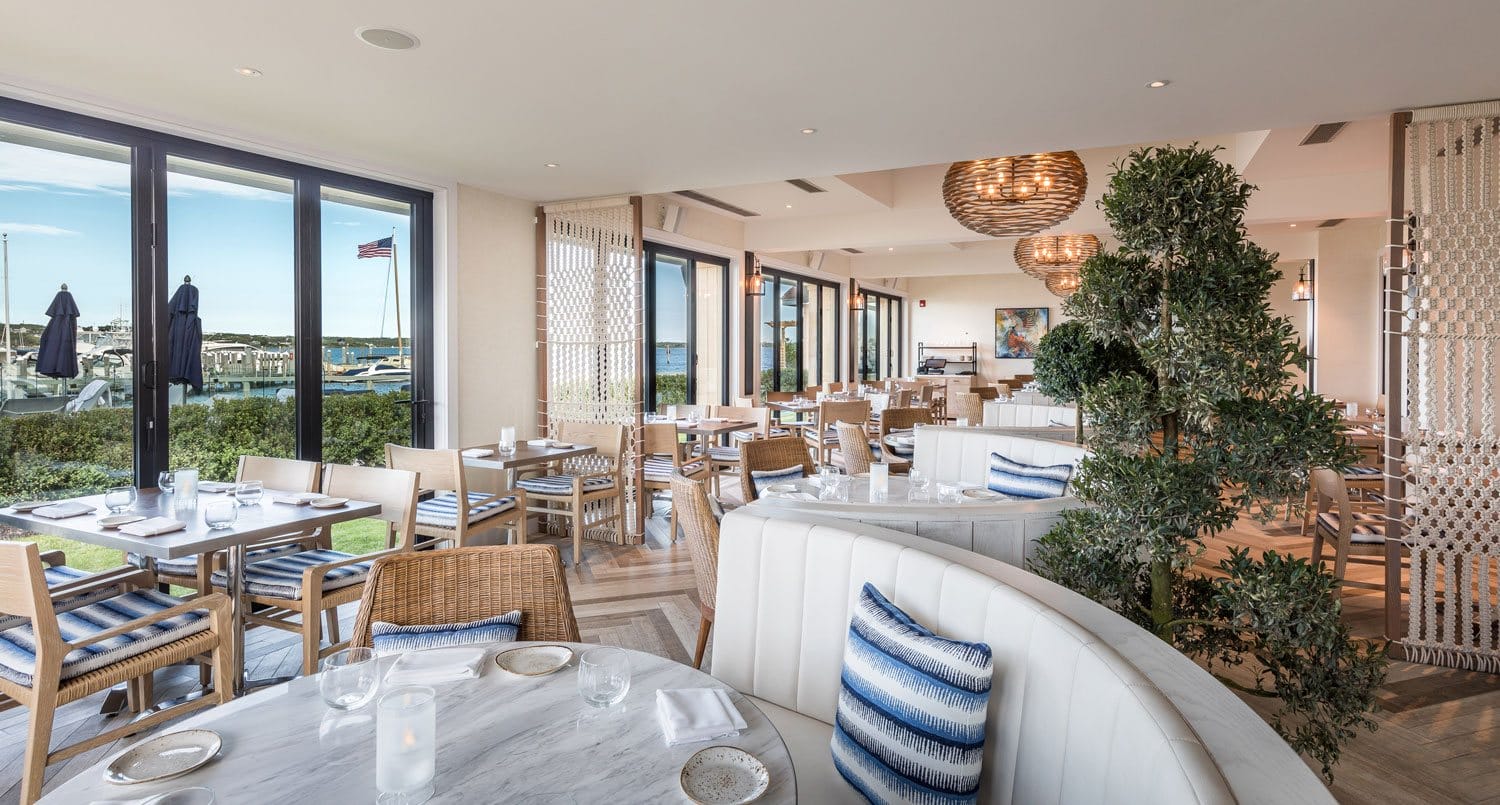 Modern restaurant interior with elegant decor, blue and white seating, large windows, and a view of the outdoors.