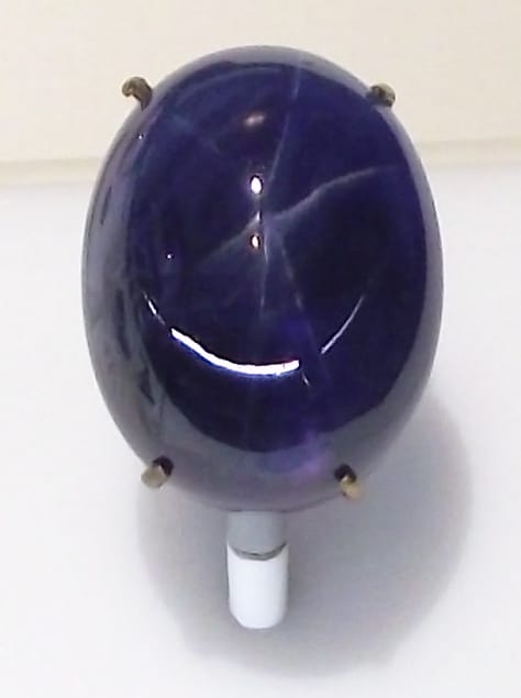 Deep blue star sapphire gemstone set in a metal prong setting on a white stand.
