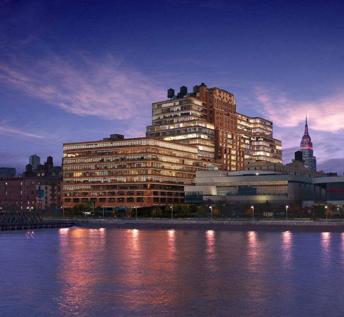 City skyline at dusk with illuminated buildings reflecting on the water.