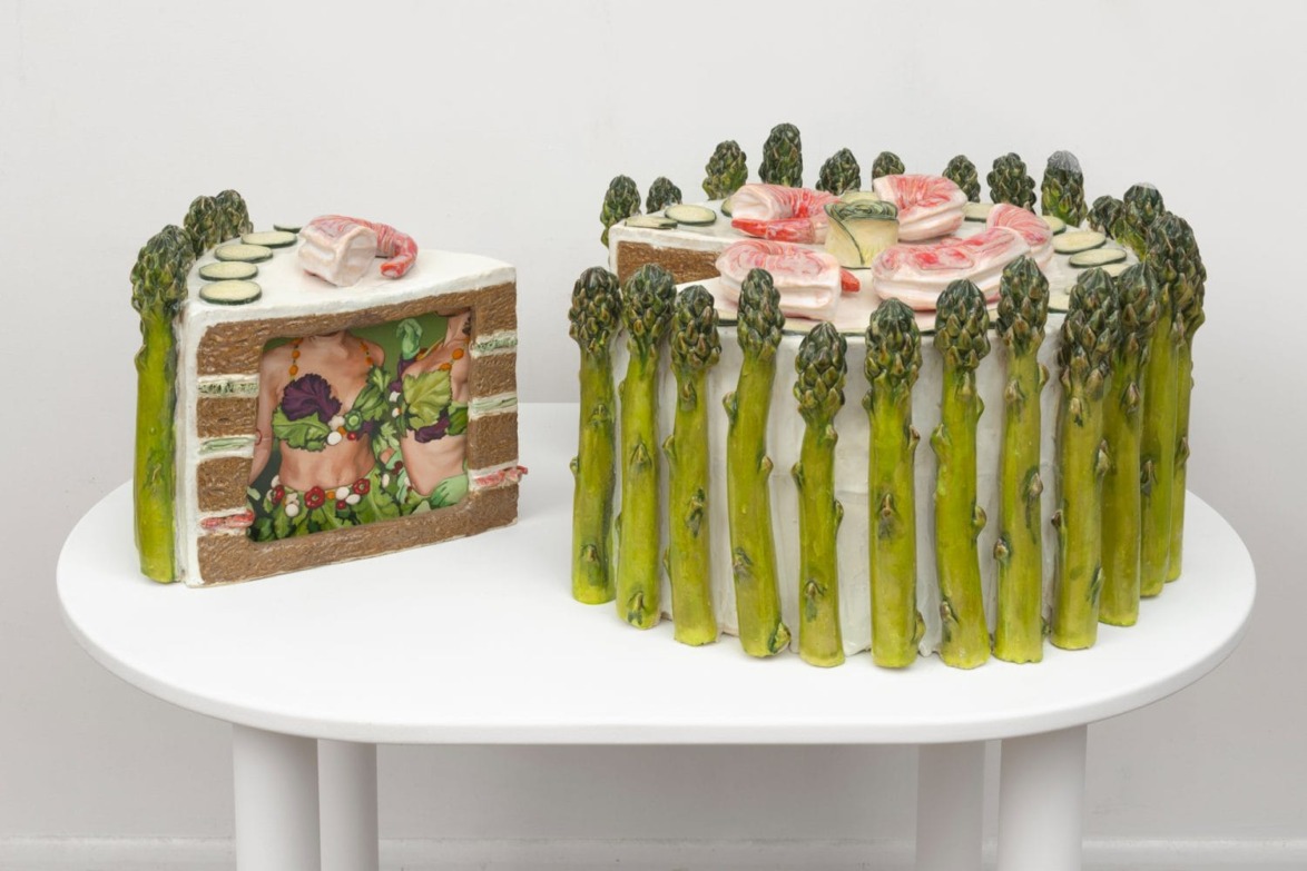 Cake sculpture resembling vegetables and meat, with asparagus exterior, on a white table.