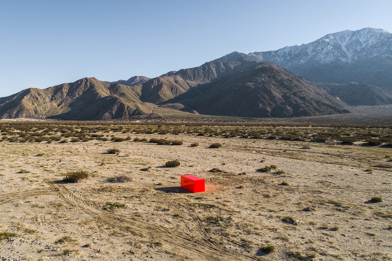 Red cube in a desert landscape with mountains in the background under a clear blue sky.