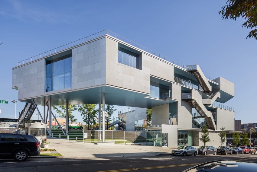 Modern building with cantilevered design, large windows, external staircases, and surrounding trees in urban setting.