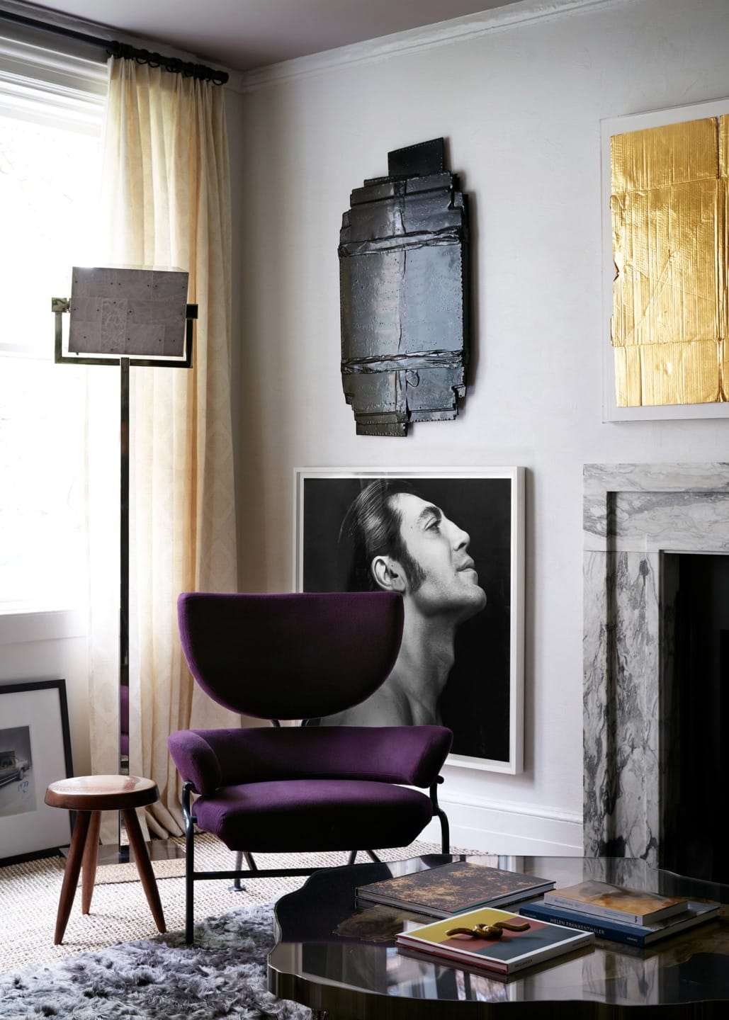 Modern living room with purple chair, abstract art, and black-and-white portrait of a person on the floor near a fireplace.