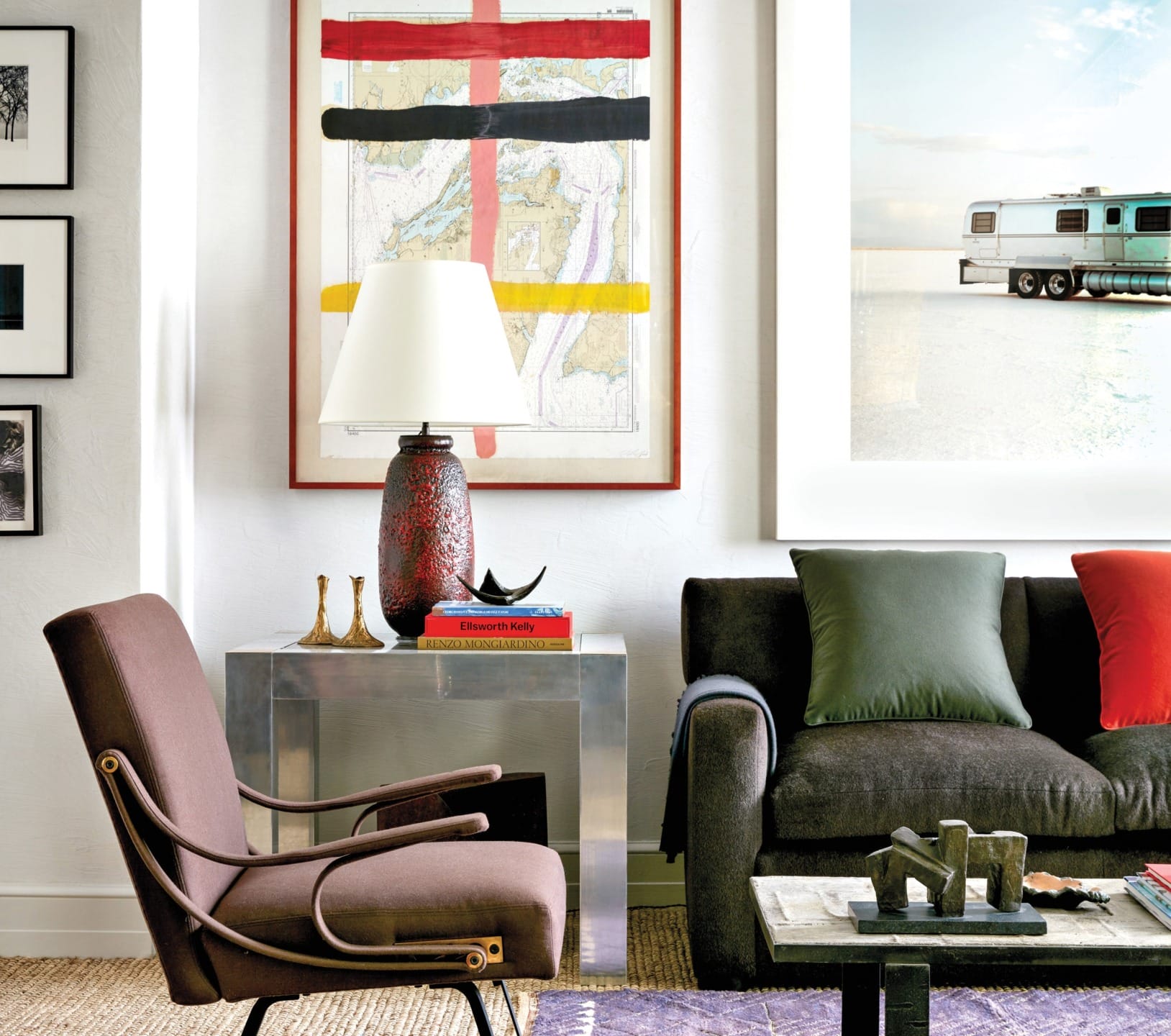 Modern living room with brown armchair, dark sofa, colorful art, lamp on metal side table, and framed photos on walls.