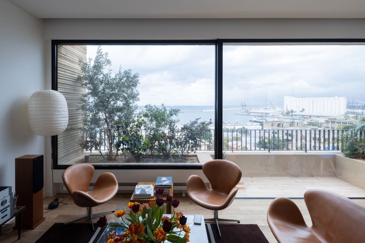 Modern living room with leather chairs, large window view of a harbor, and a vase of vibrant tulips on a table.