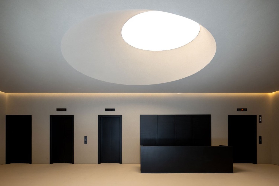 Modern lobby with three black elevators, a sleek black reception desk, and a large circular skylight on the ceiling.