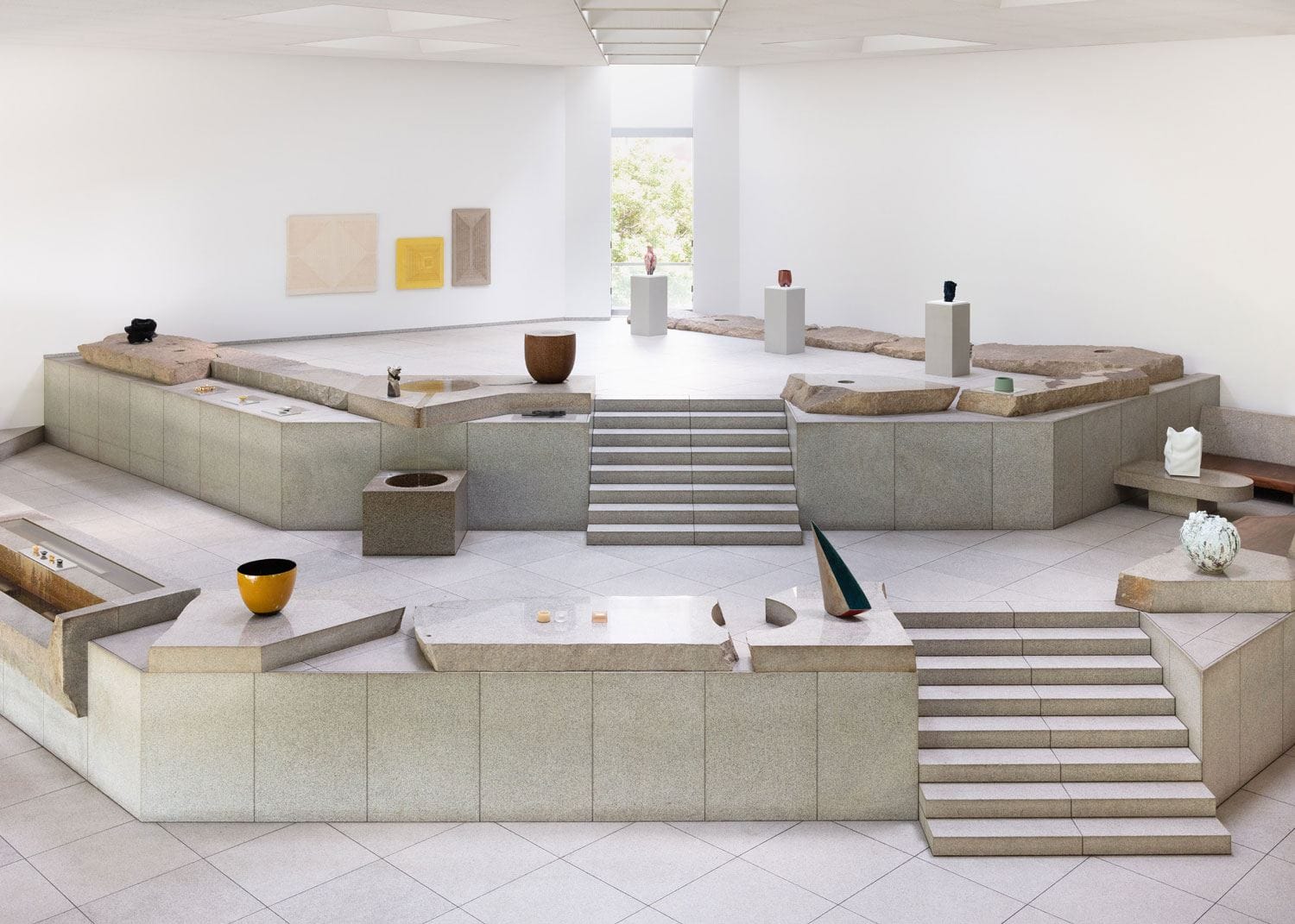 Spacious modern art gallery with geometric sculptures and minimalist artwork on display, large windows in the background.