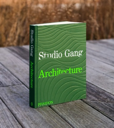 Green book titled "Studio Gang Architecture" on a wooden table with a nature background.