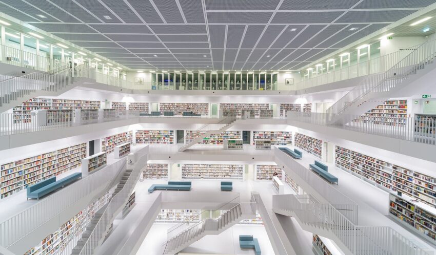 Modern library interior with multiple levels, white walls, symmetrical design, and shelves filled with books.