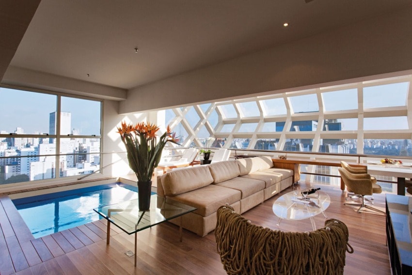 Luxurious modern living room with large windows, city view, indoor pool, beige sofa, and elegant decor elements.