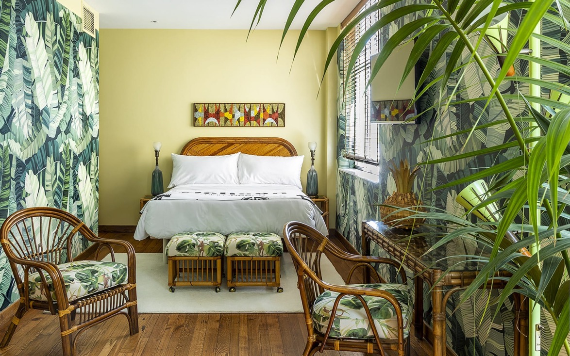 Stylish bedroom with tropical decor, wooden furniture, green leafy wallpaper, and large potted plant near a window.