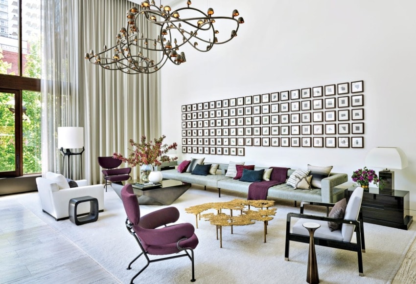 Spacious modern living room with high ceilings, abstract chandelier, art wall, and a mix of white and purple furniture.