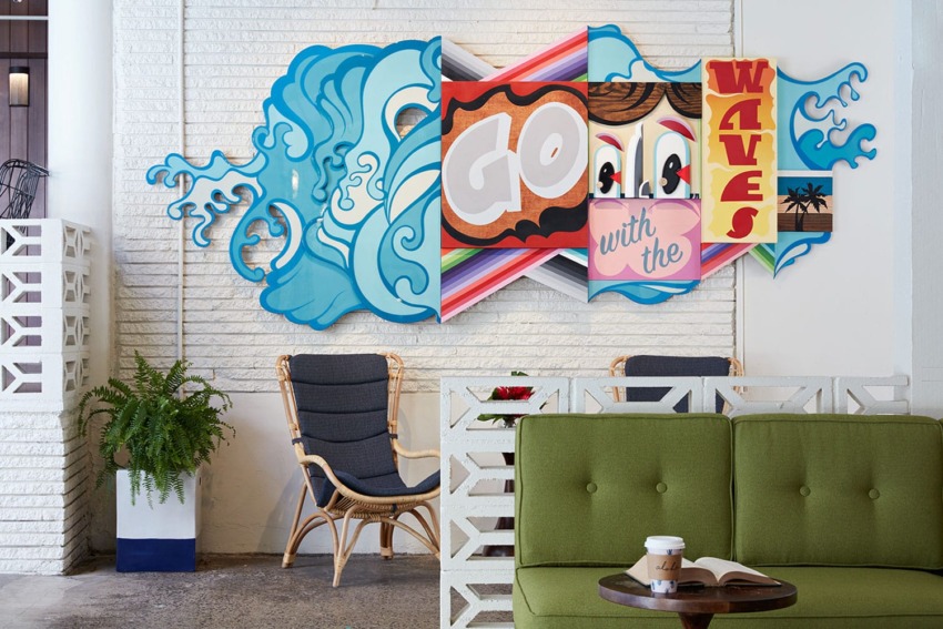 Colorful wall mural with ocean waves, text "Go with the Waves," chairs and a green sofa in a cozy lounge setting.