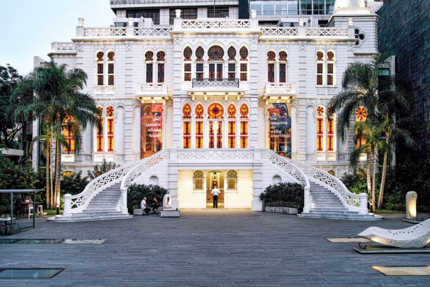 Historic white marble building with ornate windows, surrounded by palm trees, featuring grand staircases in a nighttime setting.