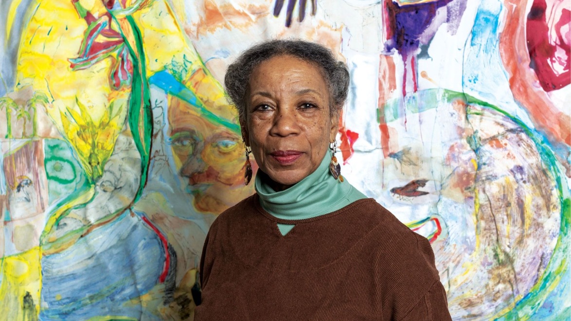 Woman standing in front of colorful abstract mural with vibrant patterns and shapes.