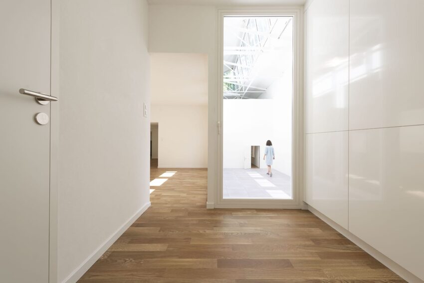 Modern interior with wooden floor, a white door, and a person walking in a bright open area in the background.