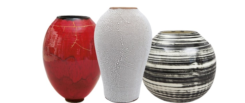 Three decorative ceramic vases, one red with gold lines, one white with a cracked design, and one black with white stripes