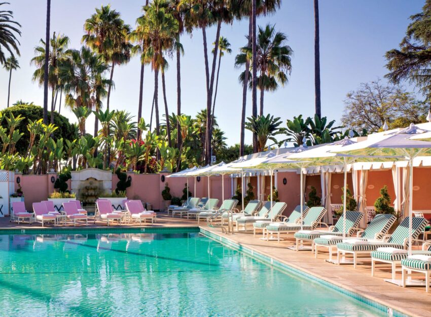 Luxurious poolside area with sun loungers, umbrellas, and palm trees under a clear blue sky.