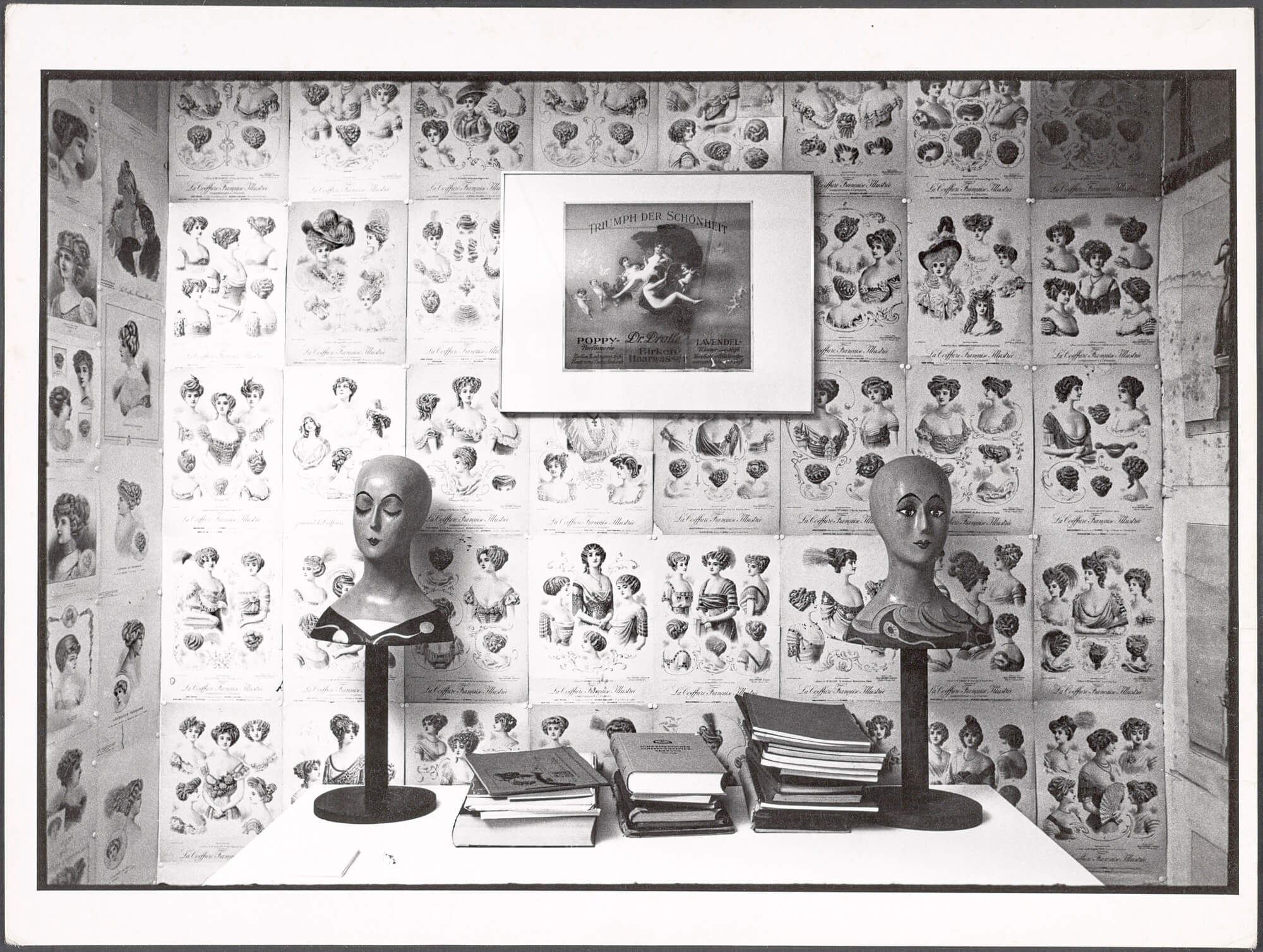 Room decorated with medical illustrations on walls, two mannequin heads on stands, and stacks of books on a table.