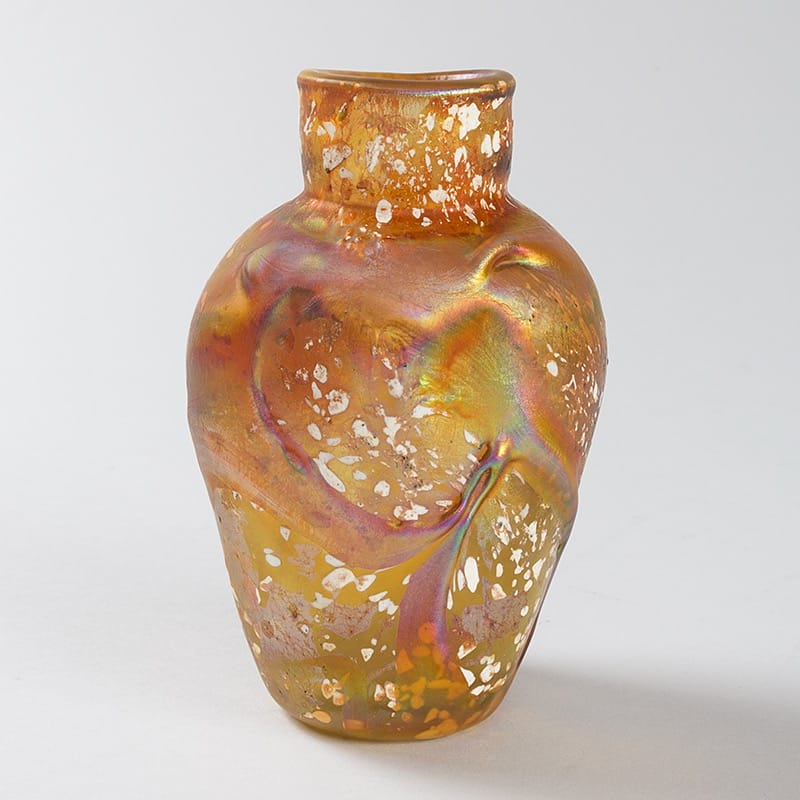 Colorful glass vase with abstract patterns and orange, yellow, and green hues on a neutral background.