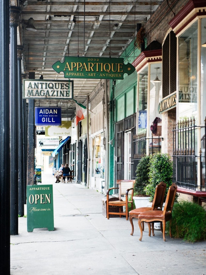 Outdoor view of an antique shop with vintage signs and furniture on a sidewalk under a wooden canopy.