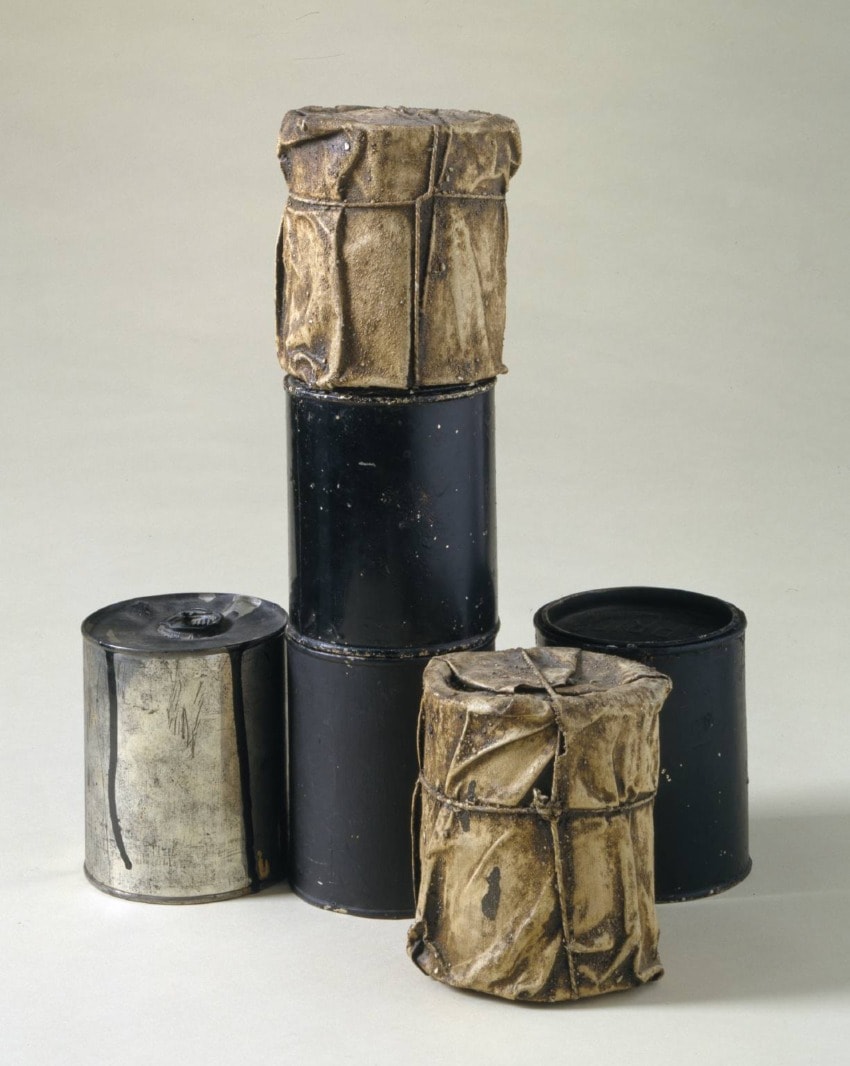 Four abstract cylindrical sculptures composed of different materials, including metal and wrapped paper, arranged together.