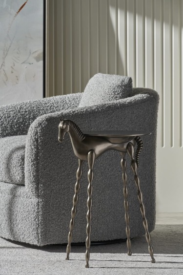 Sculptural horse table with twisted legs beside a textured gray armchair in a modern living room setting.