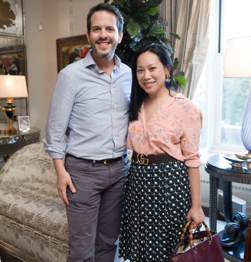 Smiling couple standing together in a stylish living room with elegant decor and a large window.
