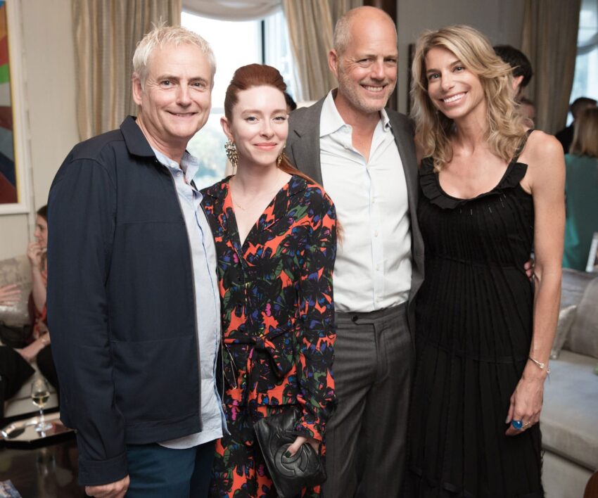Group of four people smiling and posing together in a stylish indoor setting with elegant decor in the background.