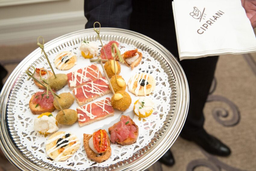 A silver platter with a variety of gourmet appetizers and a hand holding Cipriani napkins.