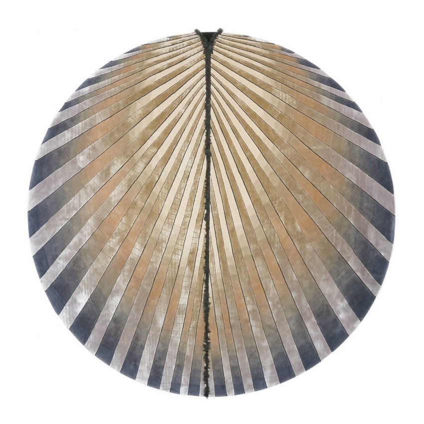 Circular artwork with radial pattern in shades of gray and beige, resembling a fan or shell design, on a white background.