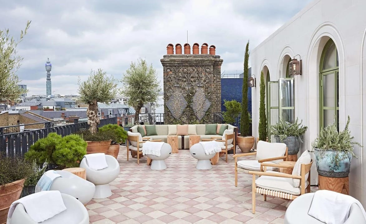 Rooftop terrace with modern seating, potted plants, and skyline view under a cloudy sky