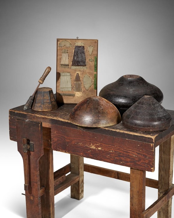 Wooden workbench with molds, a shaving tool, and sewing pattern samples on display against a neutral background.